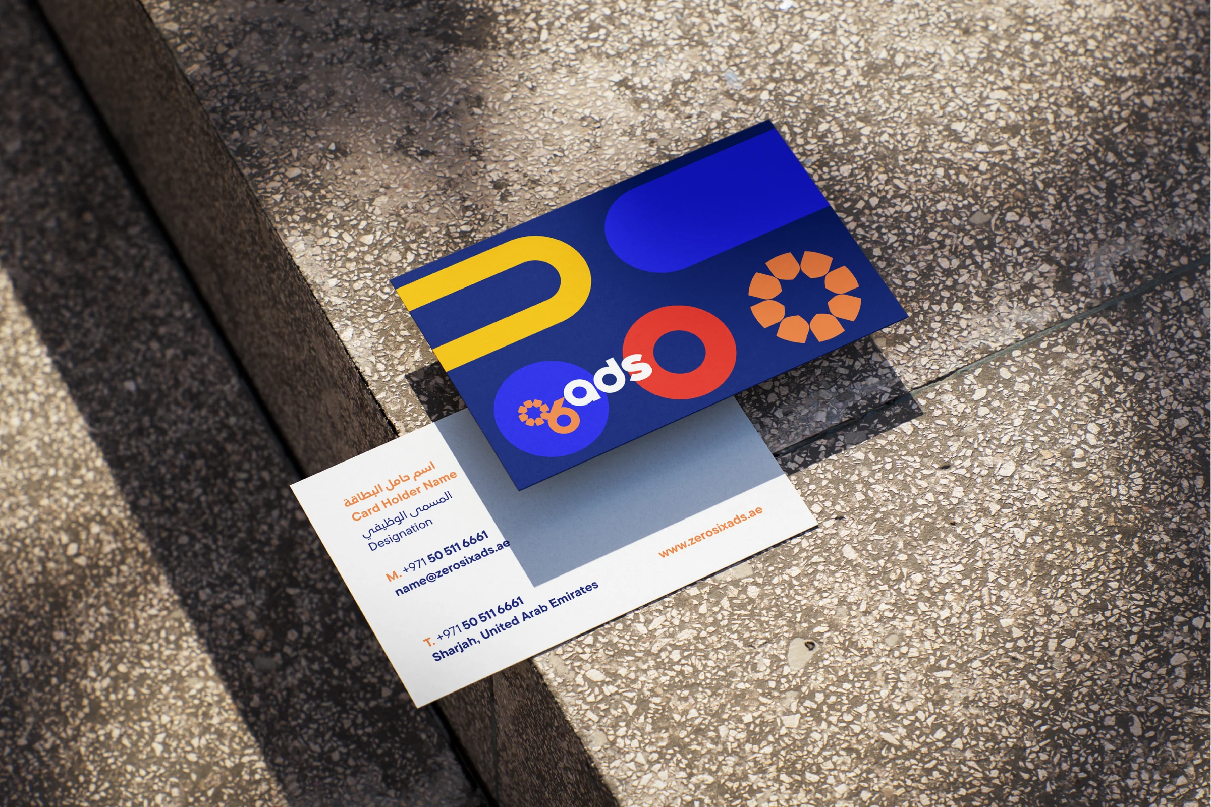 Two business cards on a terrazzo step: the back in navy with the logo and coloured shapes, the front in white with contact details.