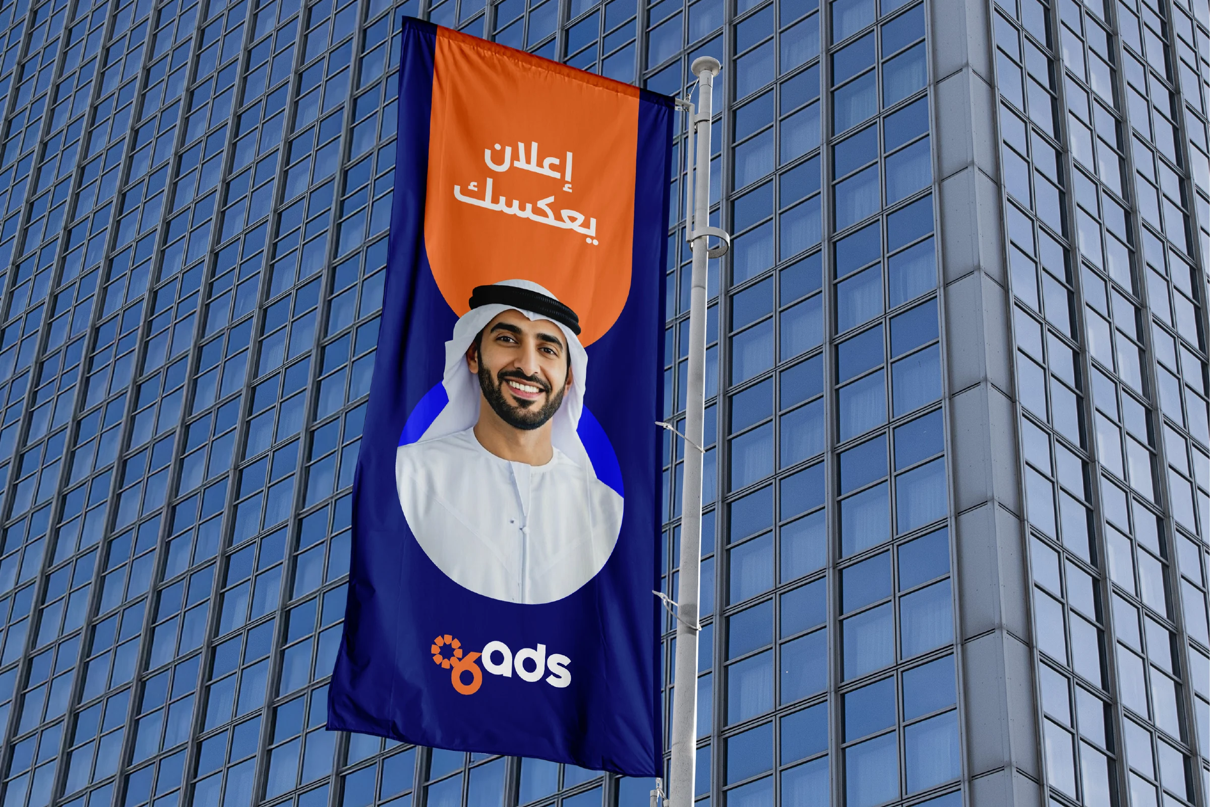 A tall flag on a glass office tower: إعلان يعكسك in white on orange over a portrait, with the logo at the bottom.