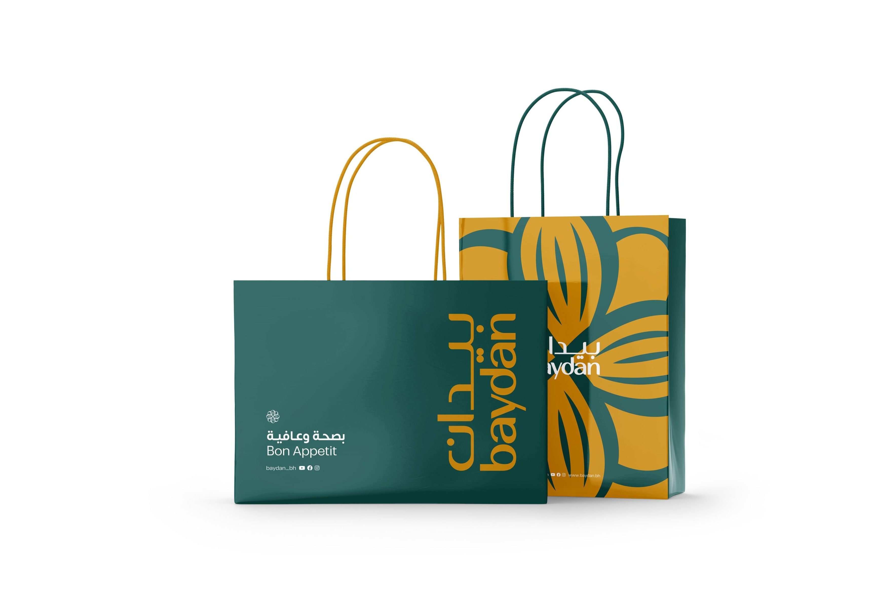 Two paper bags: a green one with the logo set vertically in gold and the line بصحة وعافية Bon Appetit, and a gold one printed with large green almonds.