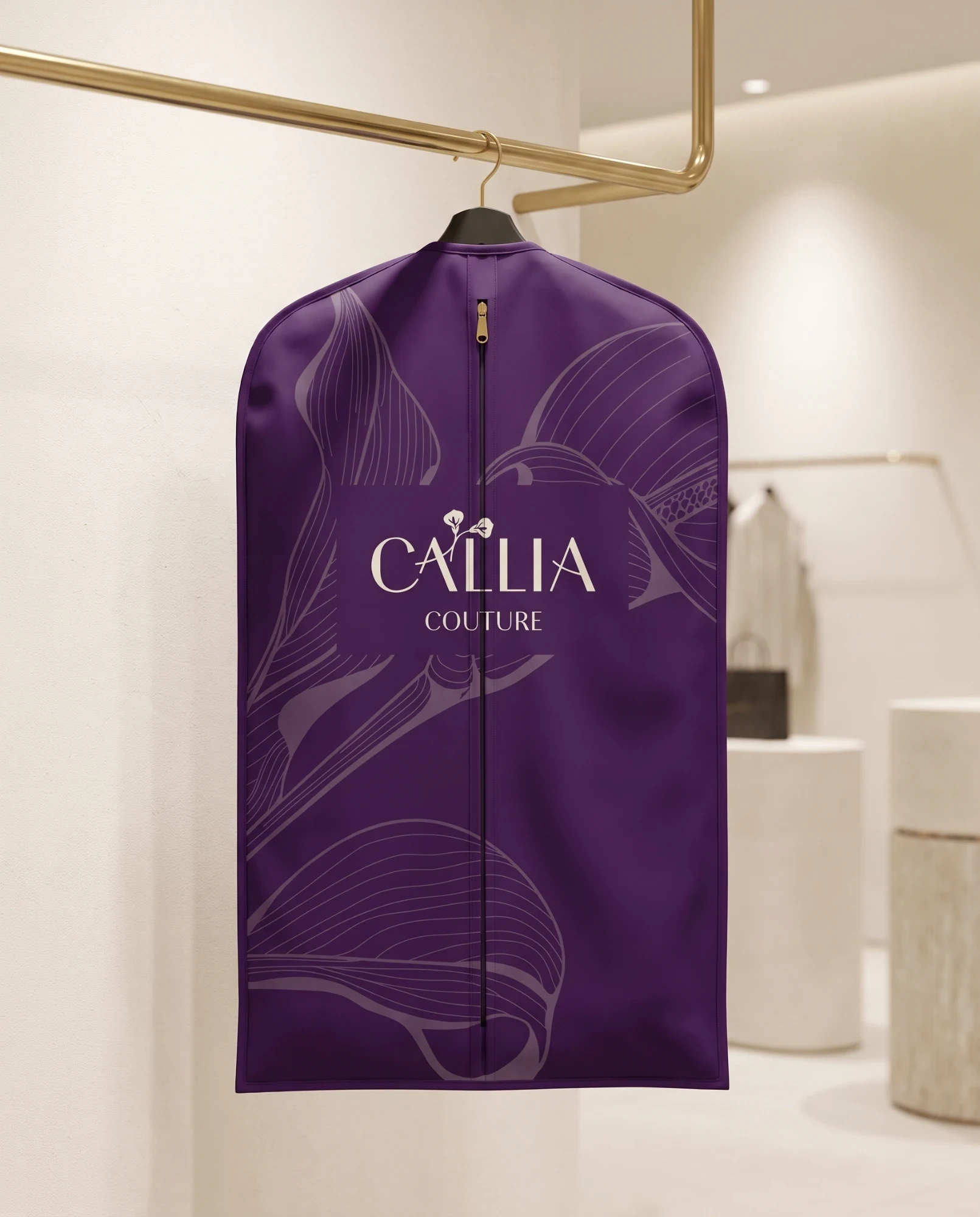 A plum garment bag hanging from a brass rail in a pale shop, printed with large lilies in a lighter plum and the logo in cream.