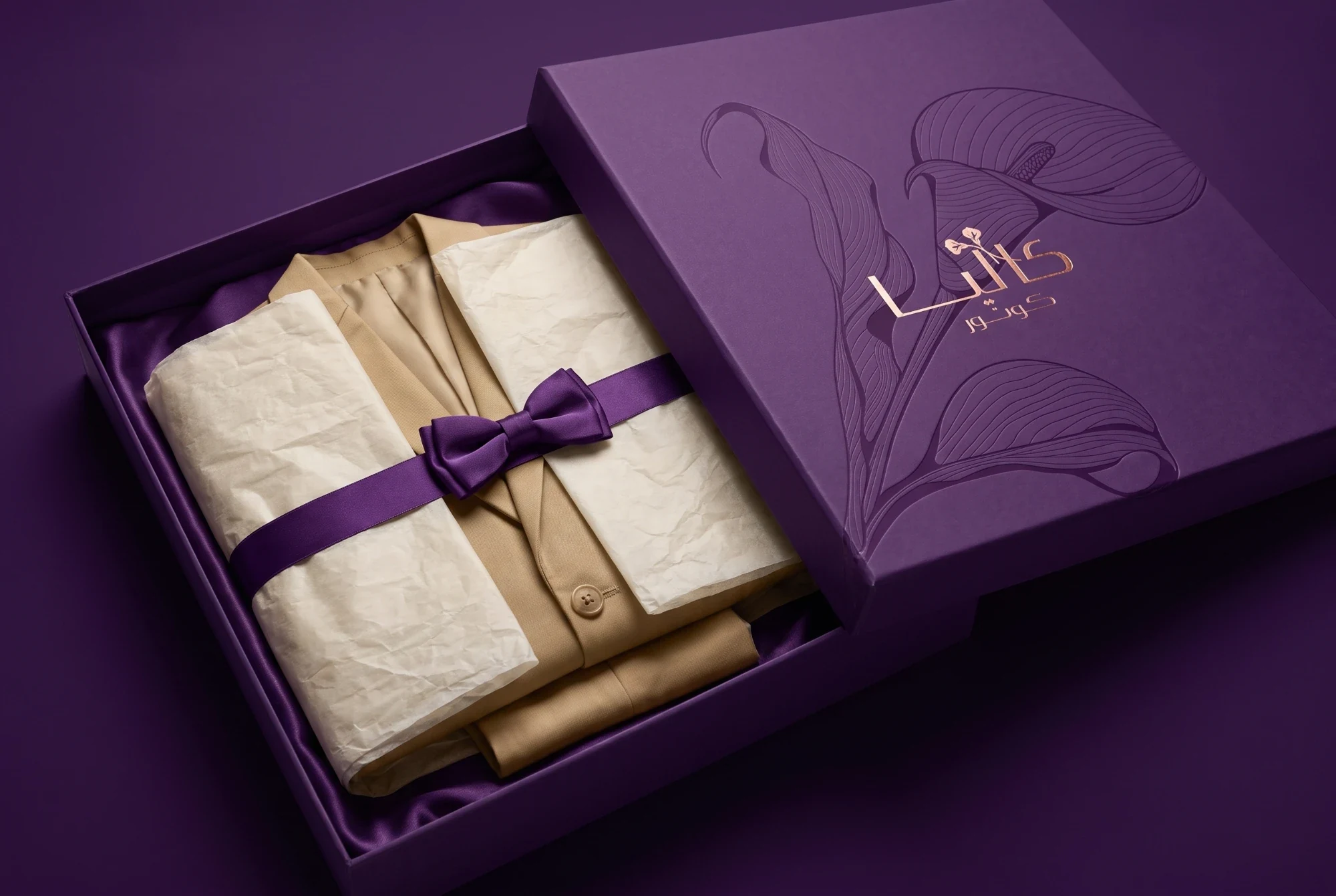 An open plum box lined with satin, holding a beige jacket wrapped in cream tissue and a plum ribbon, its lid debossed with lilies and foiled with the Arabic logo.