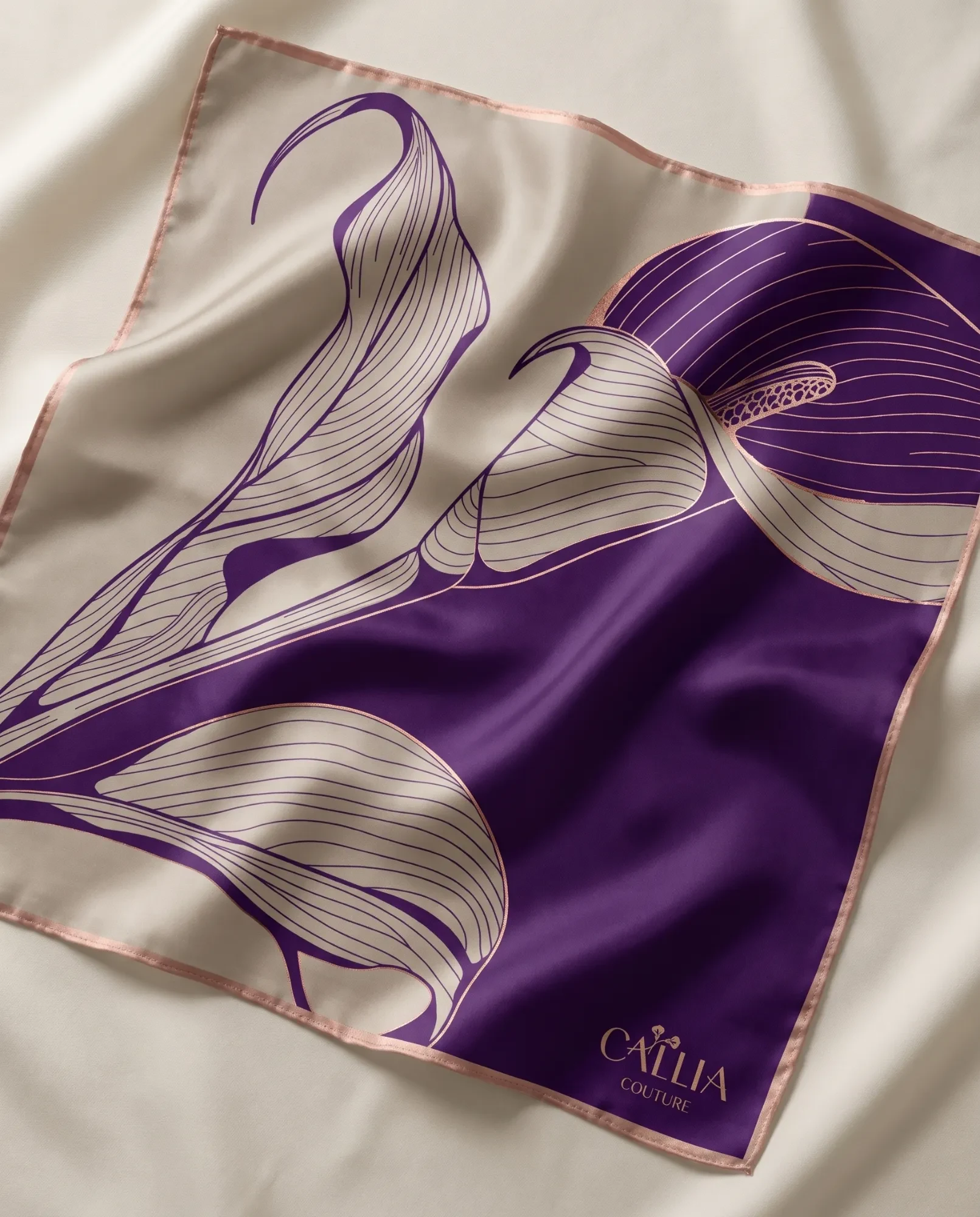 A silk square printed with large calla lilies, cream on plum and plum on cream, edged in rose gold, with the logo in one corner.