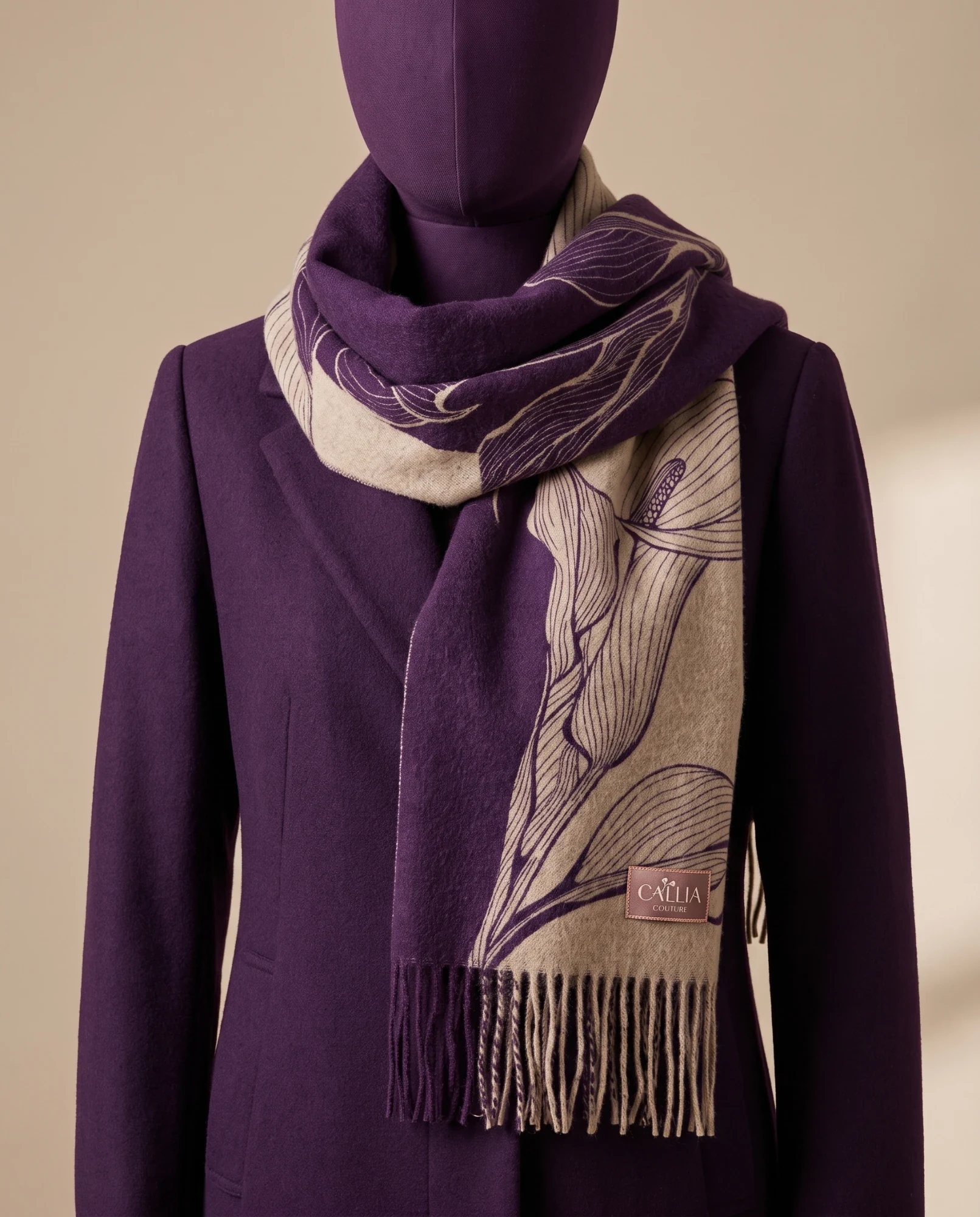 A fringed wool scarf woven with the lilies in cream and plum, with a small rose label, wrapped around a plum mannequin in a plum coat.