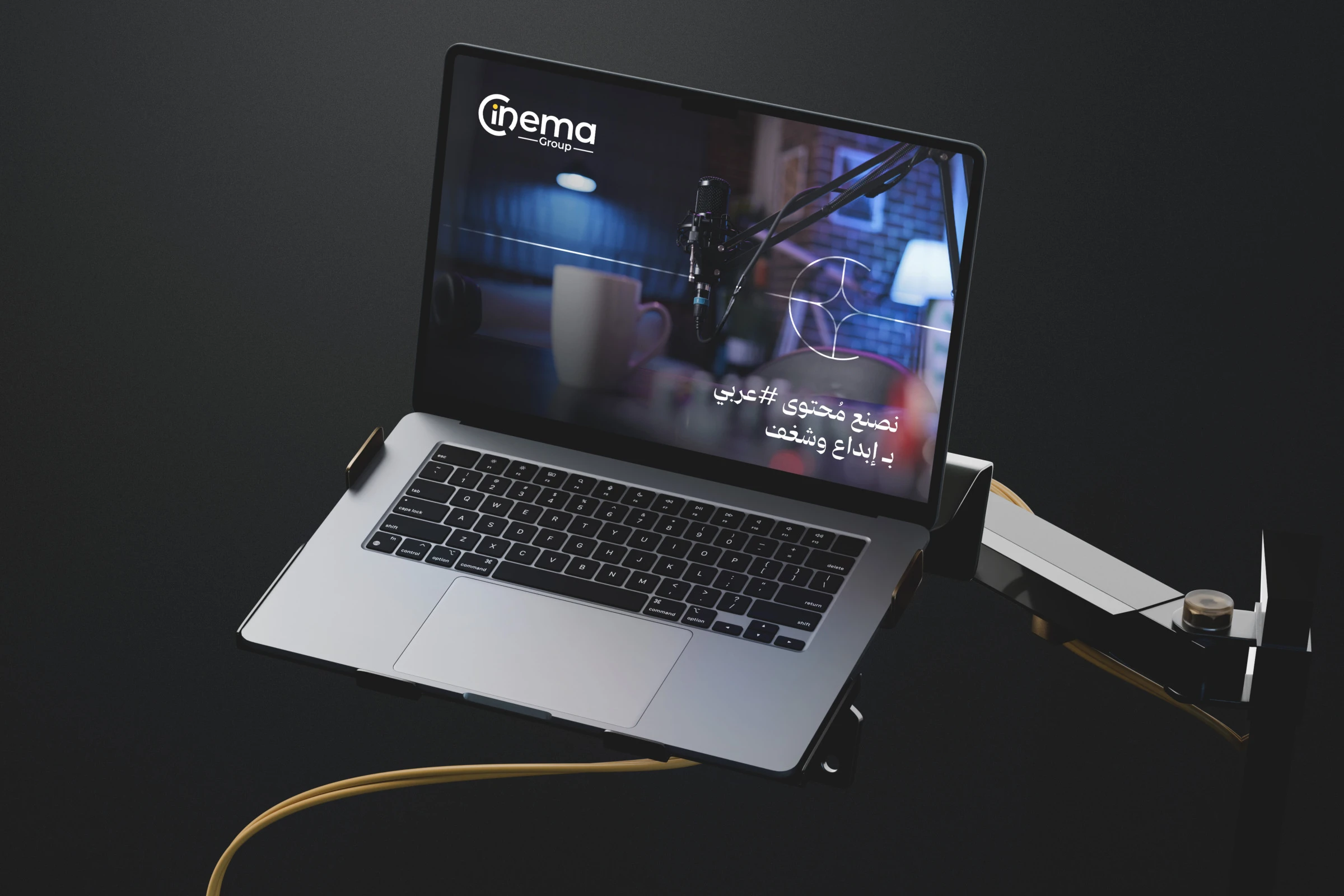 A laptop on a desk arm showing a page with the logo over a dark studio scene and an Arabic headline.