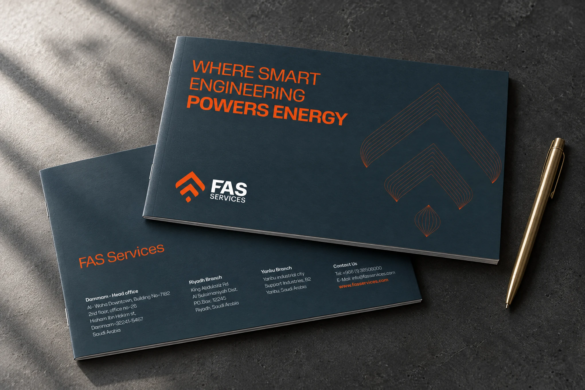 Mockup of the printed profile: the slate front cover with Where Smart Engineering Powers Energy and the FAS Services logo, over a second copy showing the back cover with the Dammam, Riyadh and Yanbu addresses, on dark concrete beside a brass pen.
