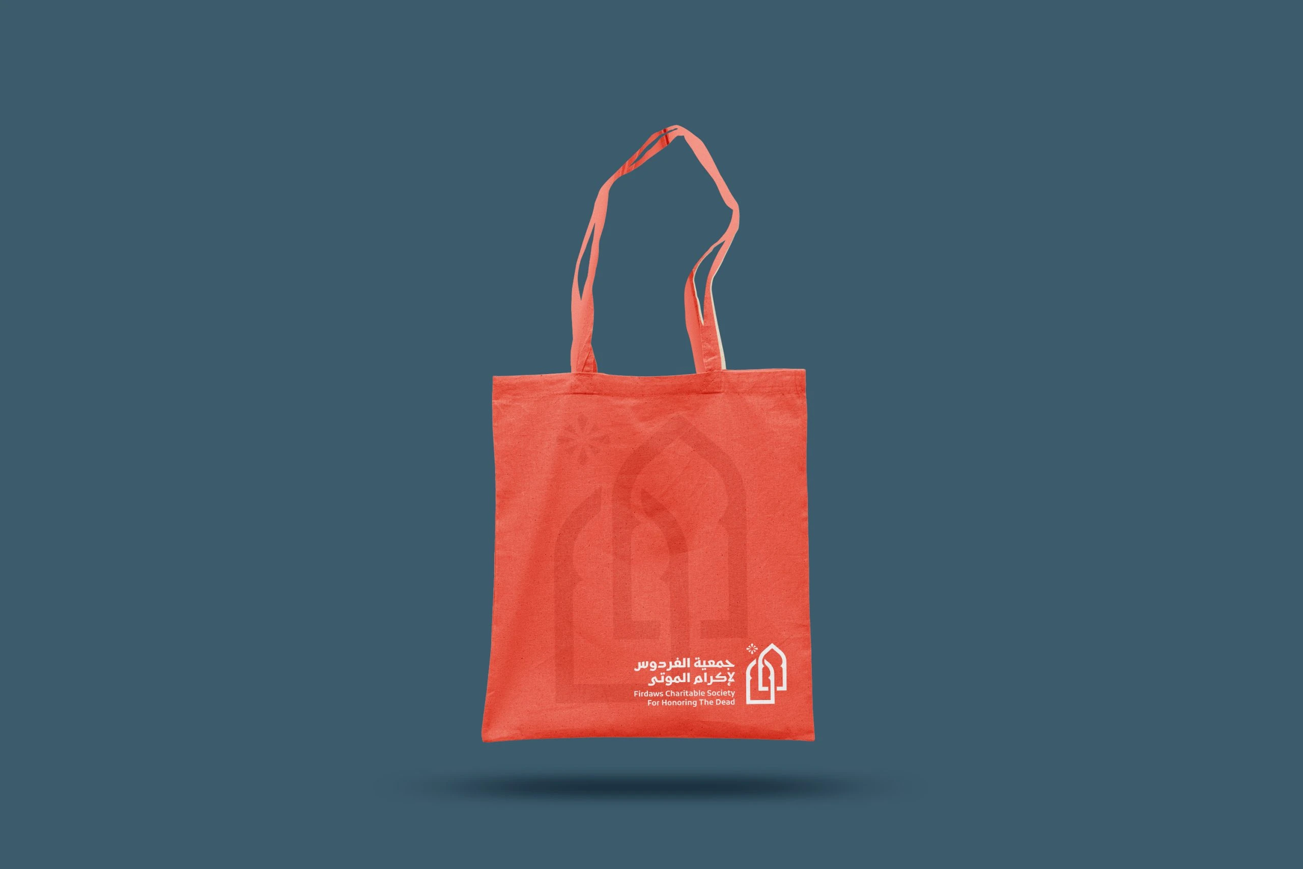 A coral tote bag with the arch and the logo, on slate.