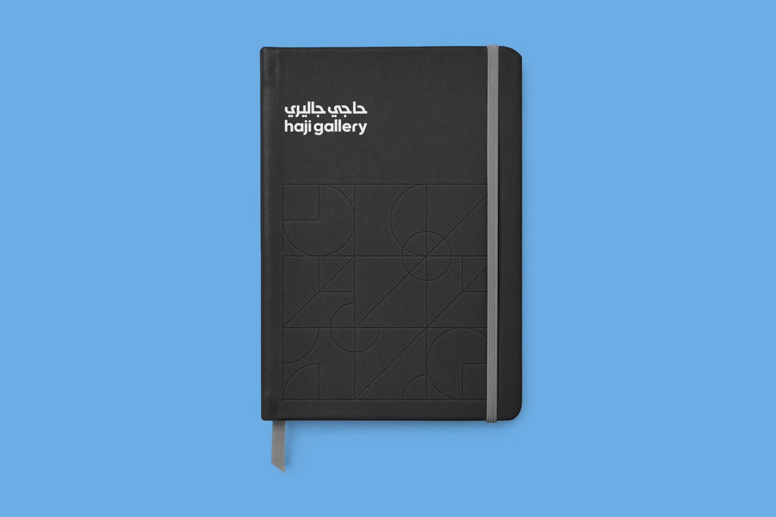 A black notebook with the logo in white and the line pattern embossed on its cover, on the brand blue.
