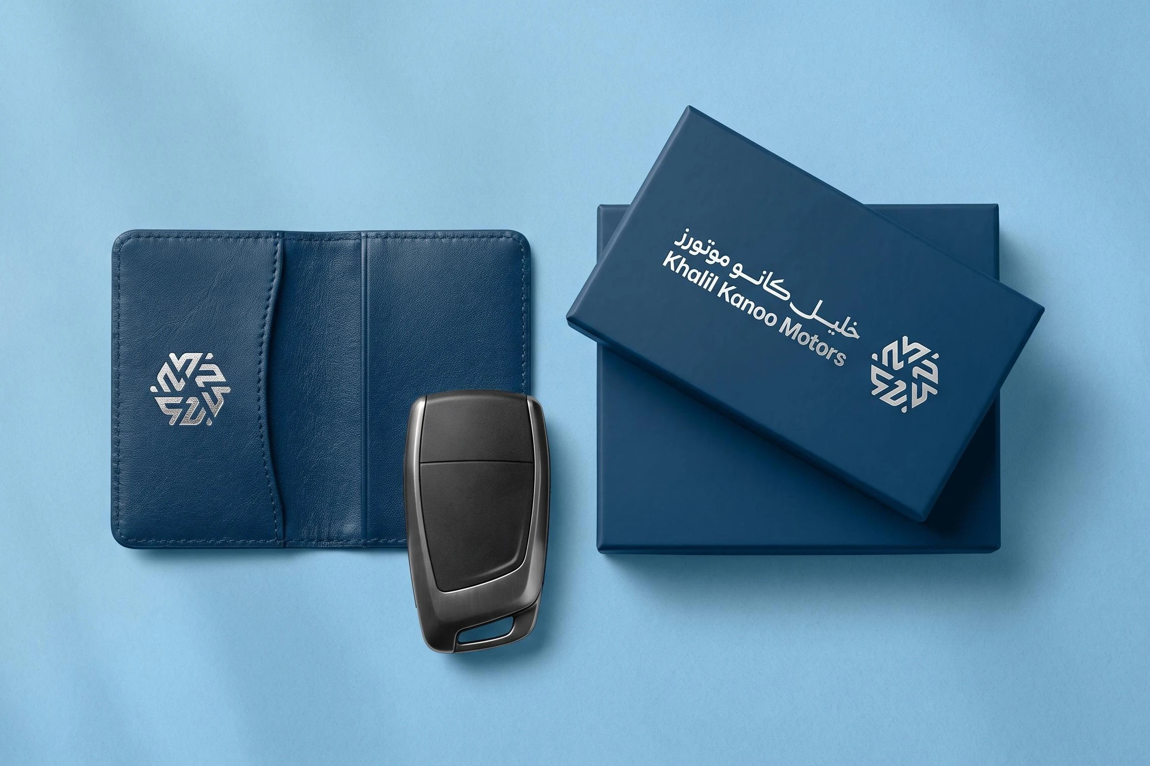 A navy leather card holder with the silver mark, a car key, and a navy box with the logo in silver, on sky blue.