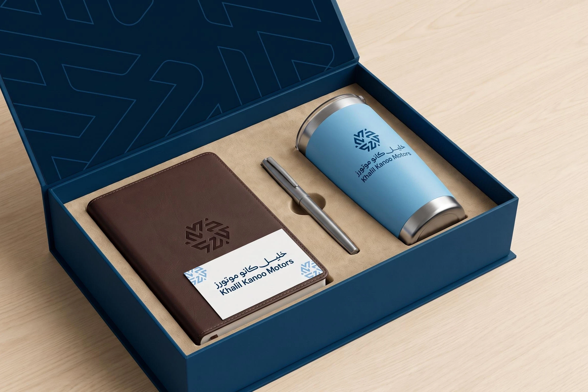 An open navy gift box lined with the mark’s strokes, holding a brown leather notebook embossed with the mark, a pen and a sky blue tumbler with the logo.