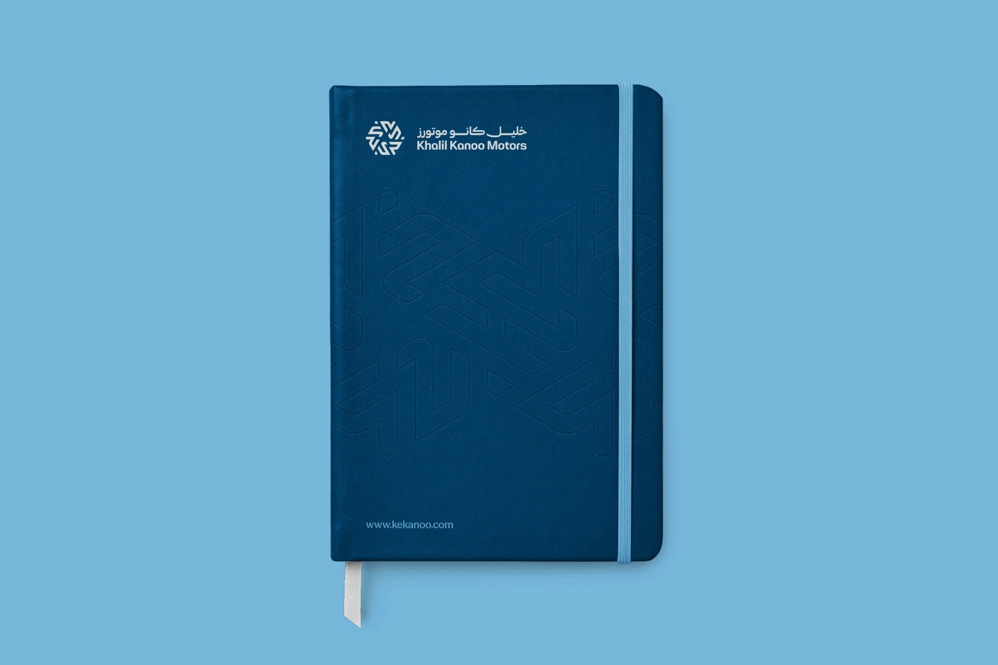 A navy notebook with the logo in white and a sky blue elastic band, on sky blue.