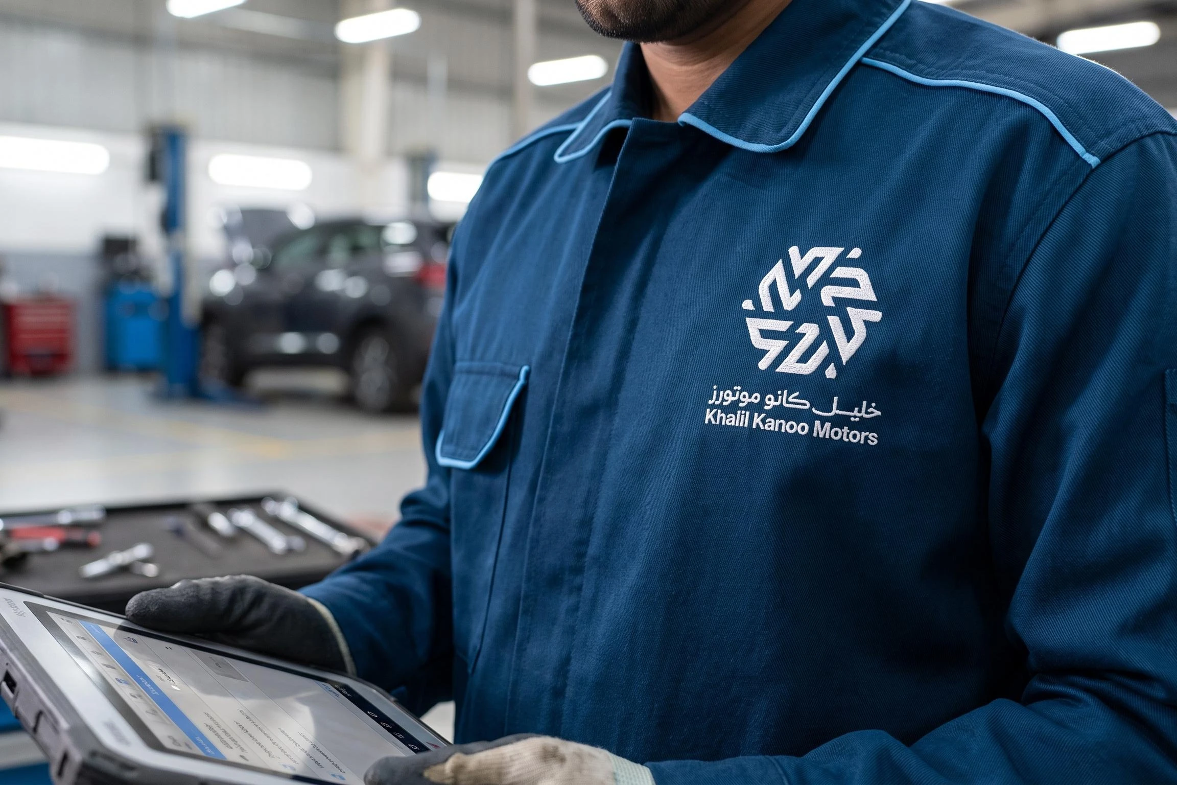 A technician’s navy jacket with sky blue piping and the logo embroidered in white on the chest, in a car workshop.