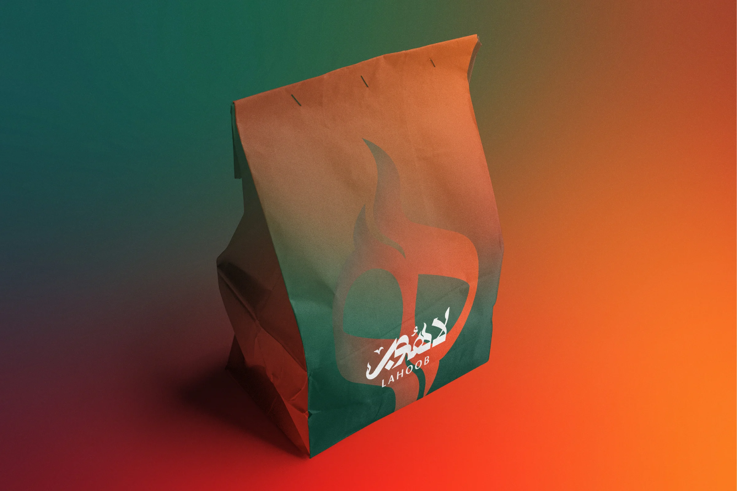 A folded paper takeaway bag, shading from orange at the top to green at the base, printed with a large flame ه and the logo in white, on an orange and green background.