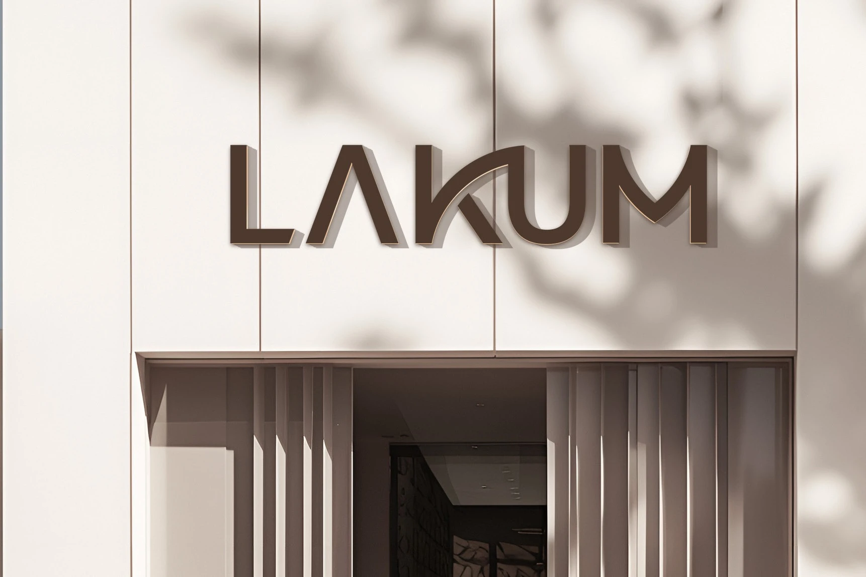 LAKUM in raised brown letters on a pale building front, above a slatted entrance, with leaf shadows falling across the wall.