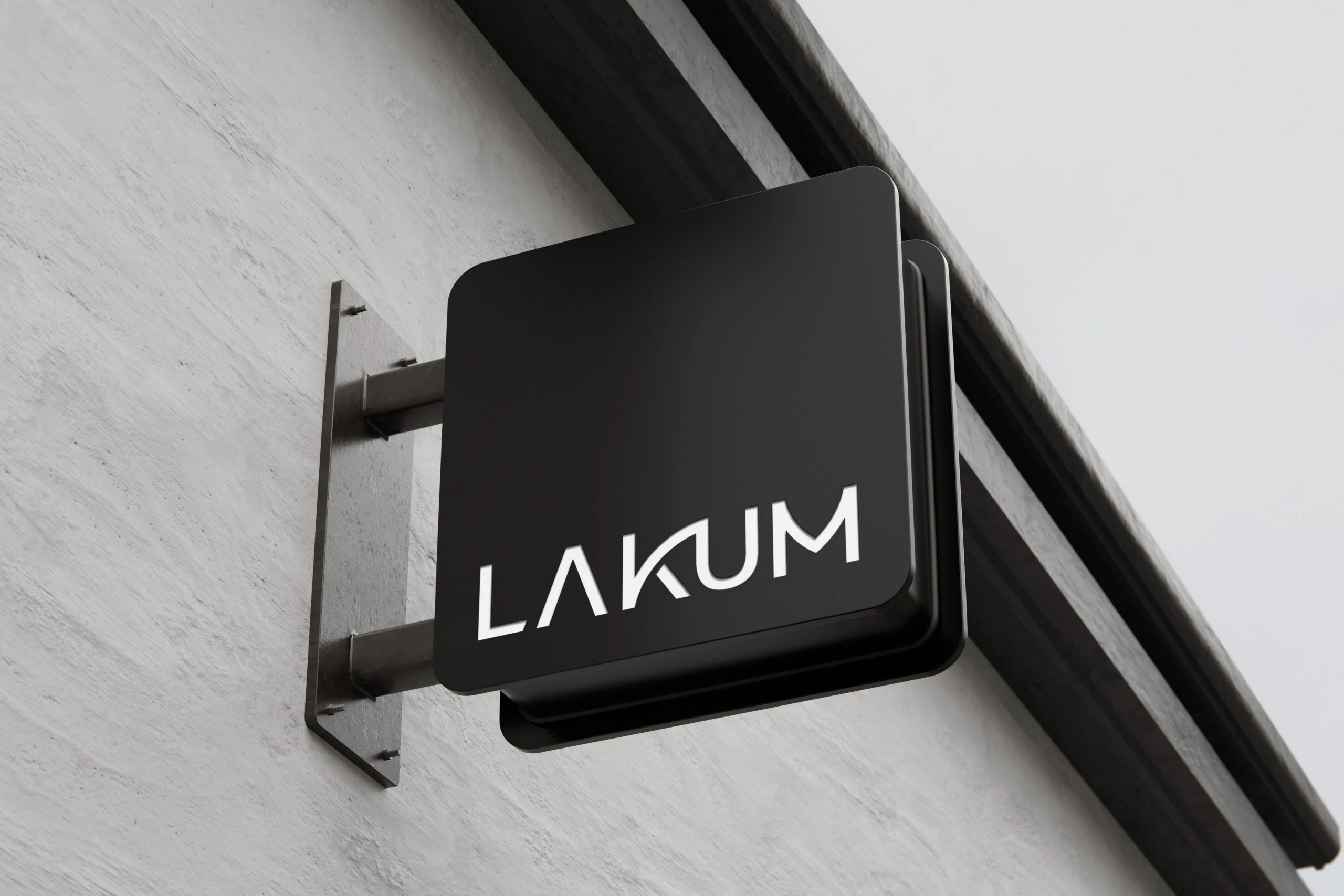 A black square projecting sign with LAKUM in white, fixed to a pale textured wall below a dark roof edge.