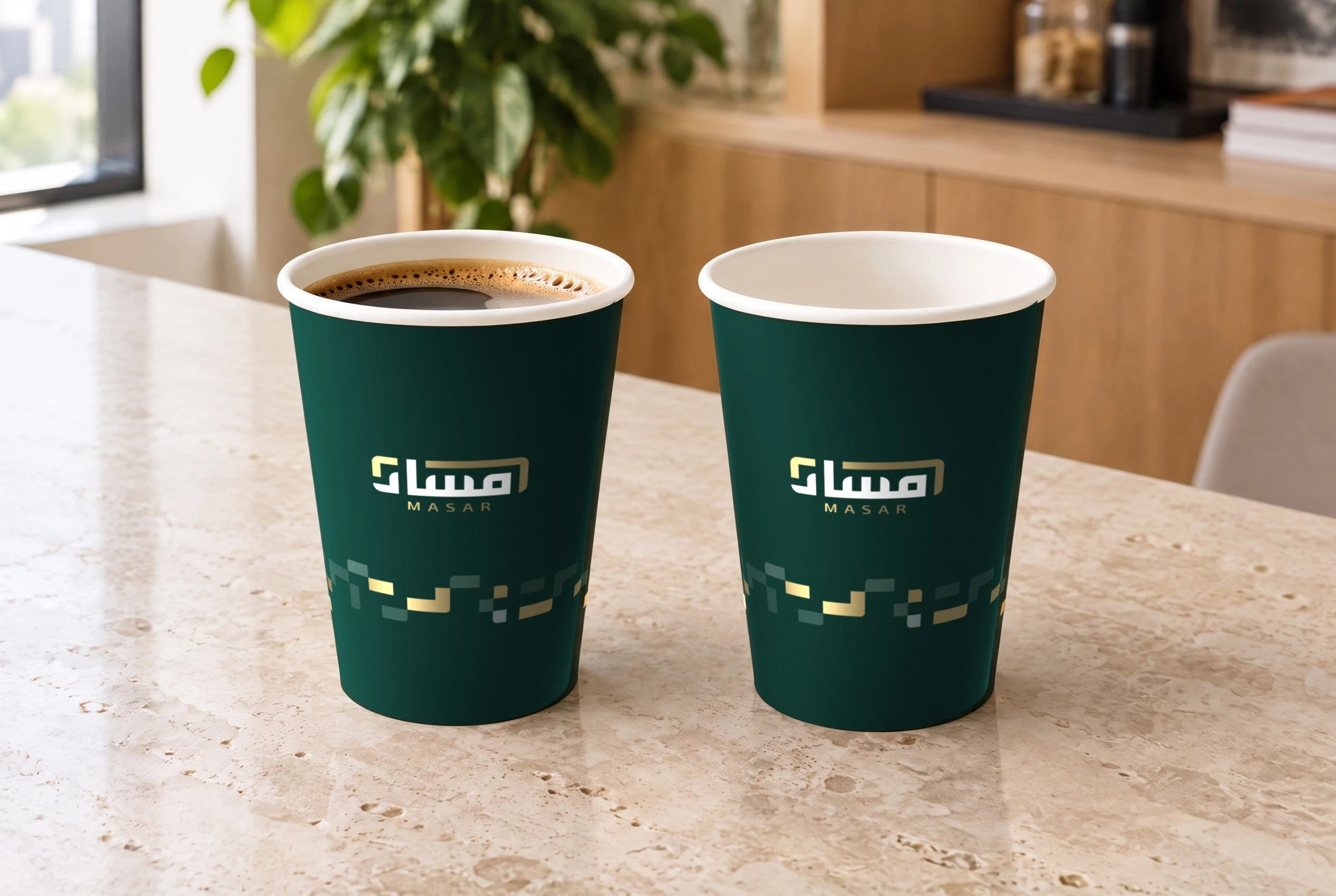 Two deep green paper cups with the Masar logo and the gold pattern on a travertine counter, one holding coffee.