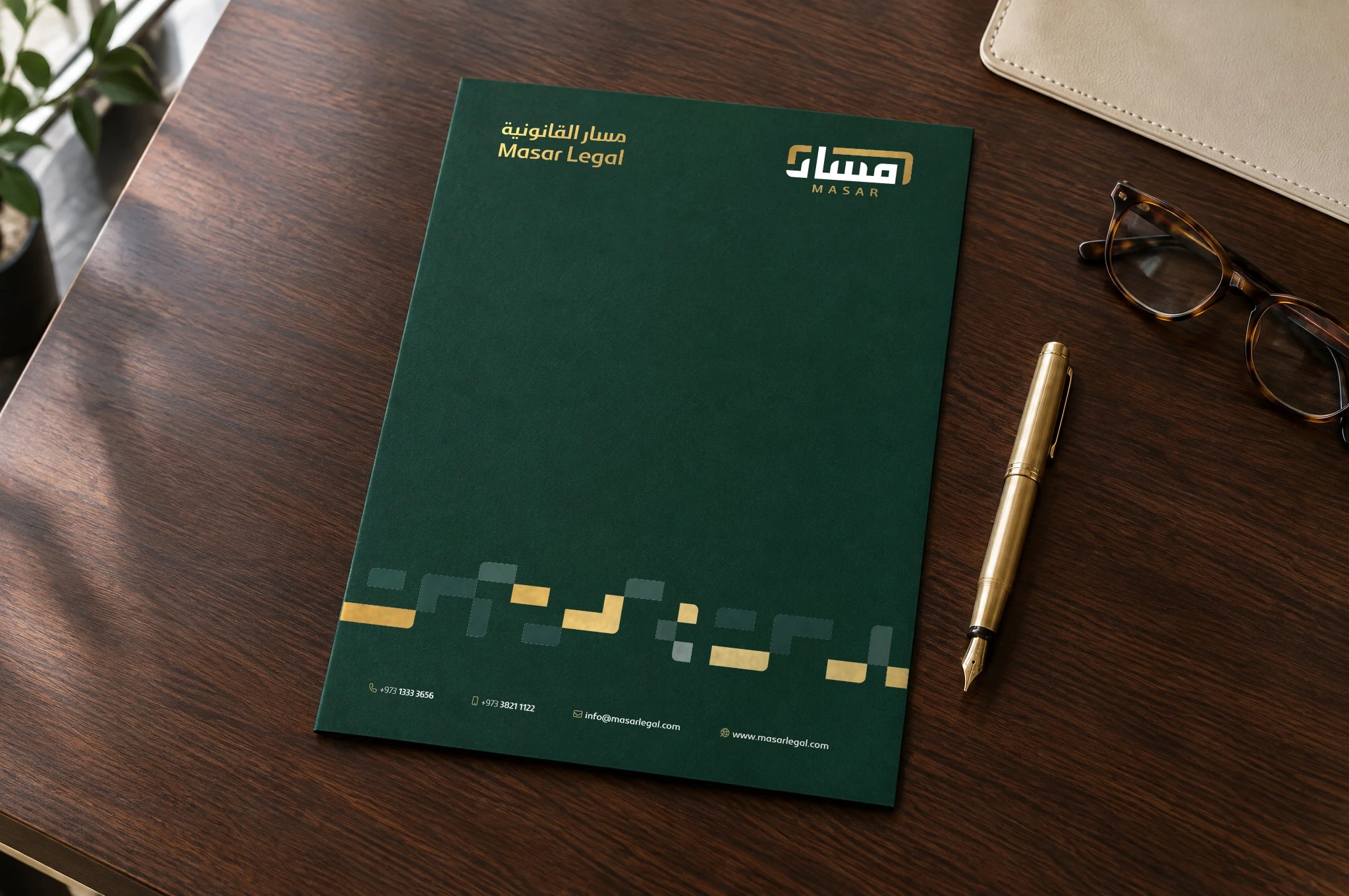 A closed A4 folder in deep green on a walnut desk, with the logotype, logo, gold pattern and contacts, beside a gold fountain pen and glasses.