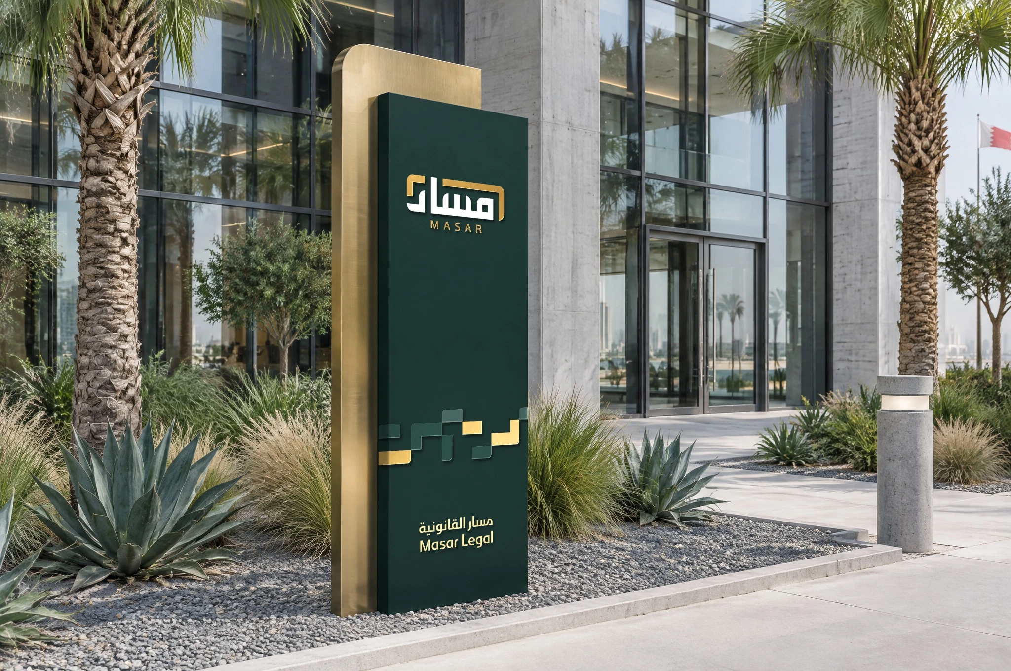 A freestanding Masar sign outside a glass office building: a deep green panel with the logo, the pattern and the logotype, in front of a brushed gold blade, among palms and agaves.