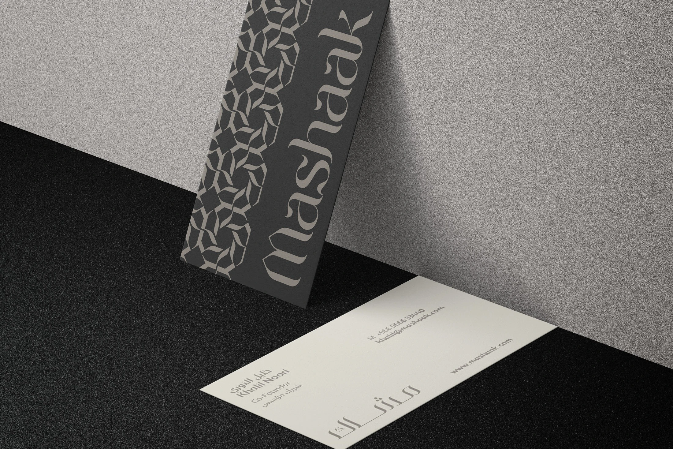 Mashaak business cards: a patterned charcoal back with the logotype leaning above a white front, on grey and black.
