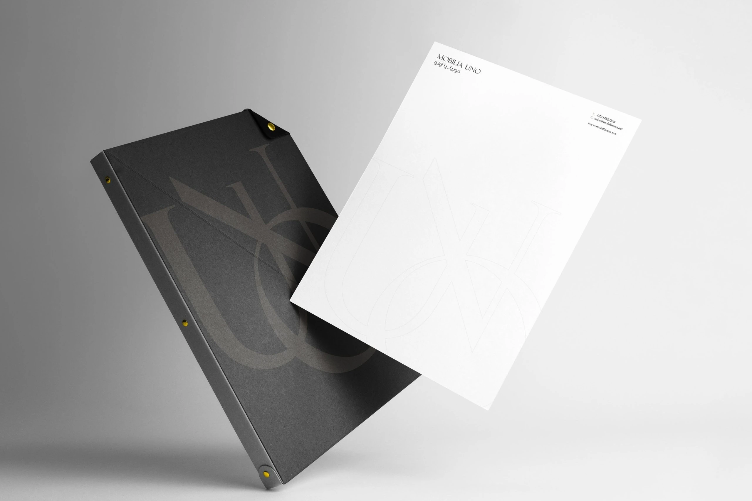 A letterhead sheet in front of a dark folder printed with the monogram, floating on a grey background.