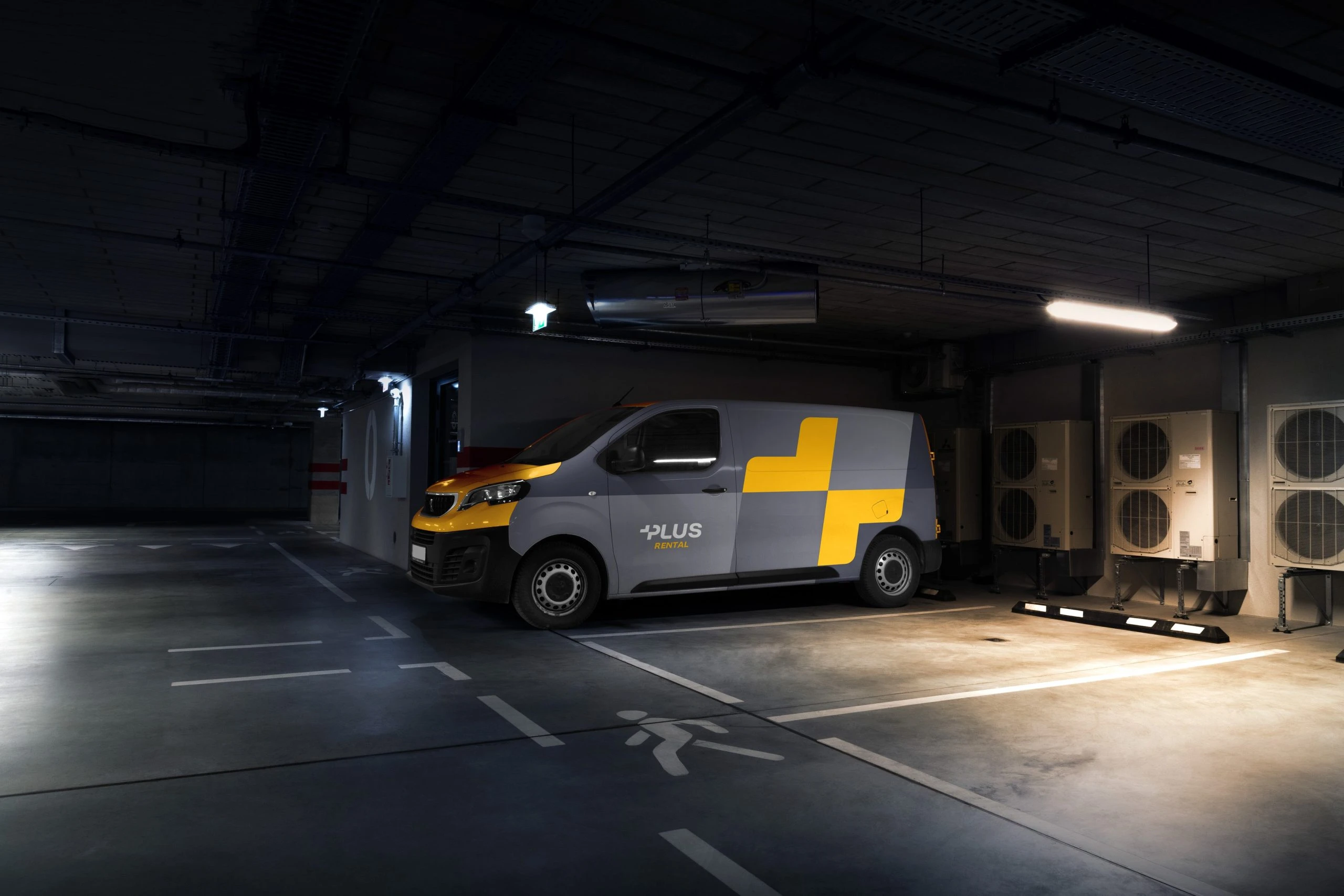A grey panel van with a yellow nose, the Plus Rental logo on the door and a large yellow split plus along its side, parked in a dim underground car park.