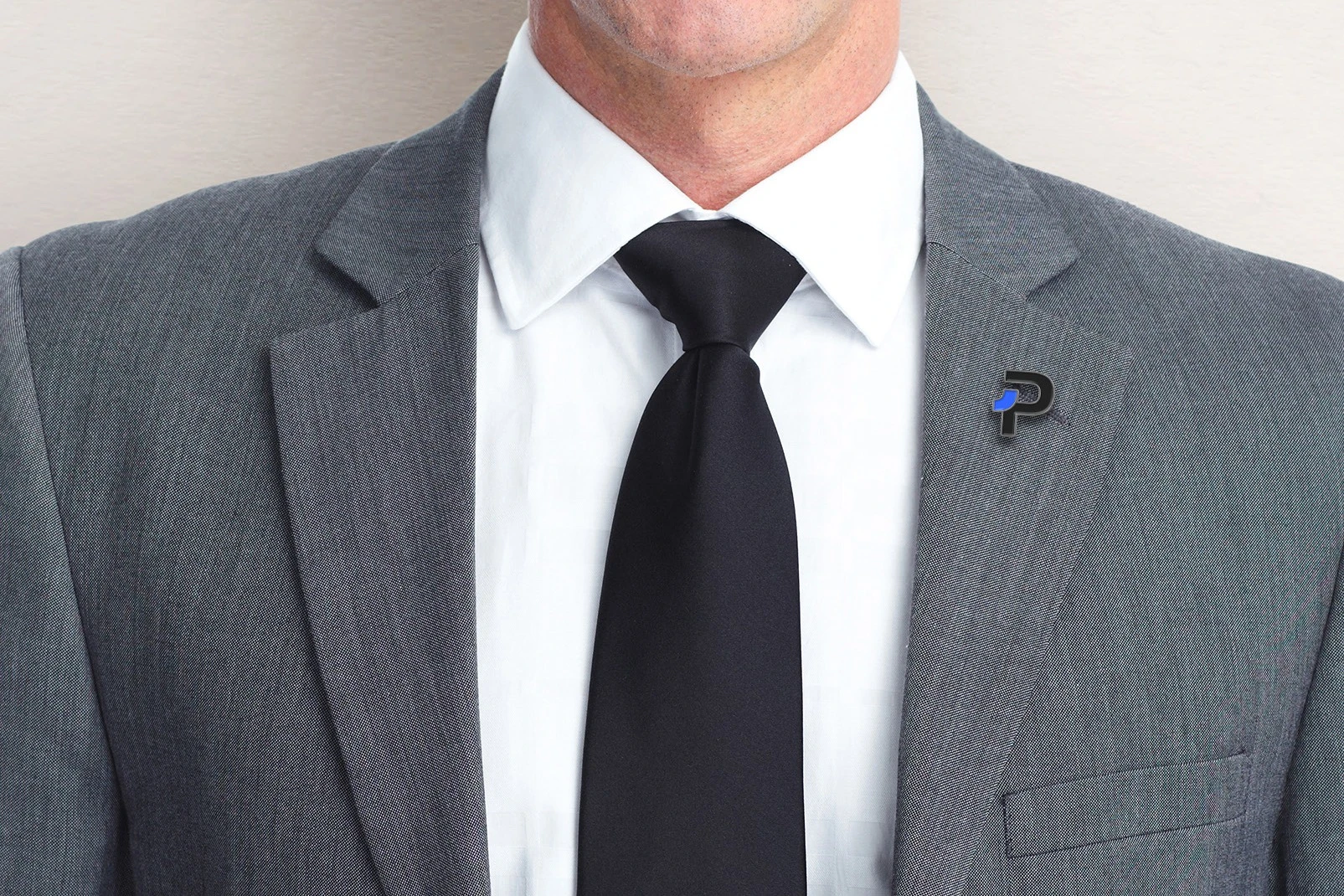 A black P lapel pin with its blue corner on the lapel of a grey suit.