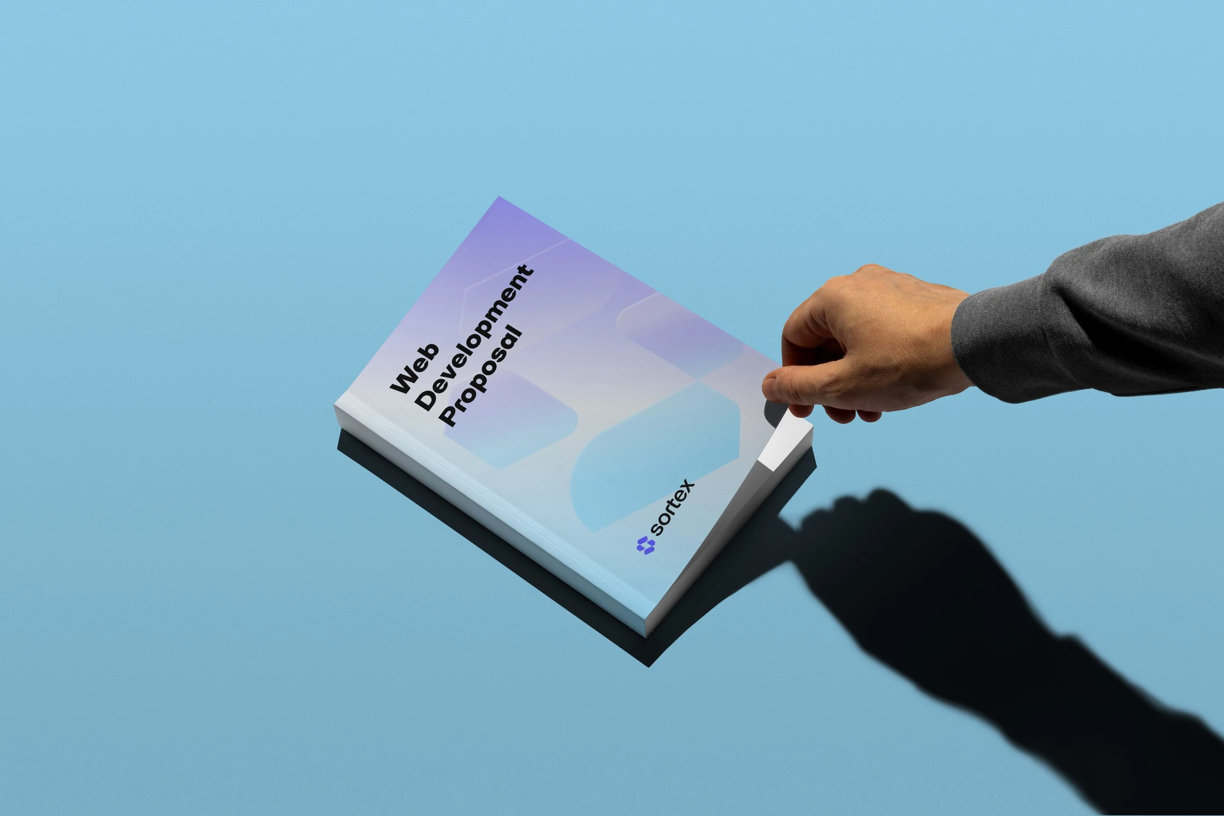 A hand opening a printed booklet with a Sortex cover in a violet to sky-blue gradient.