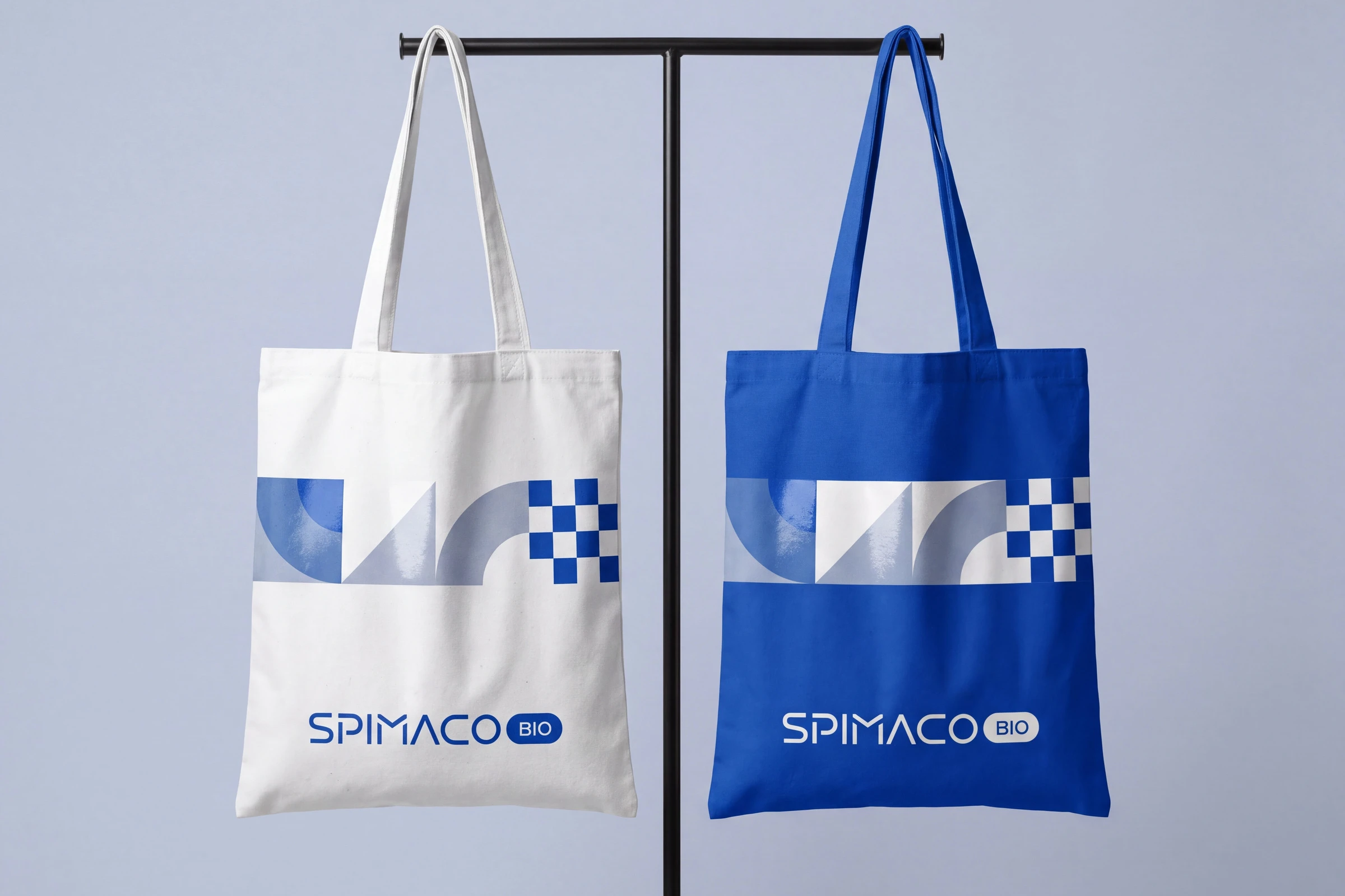 A white tote and a blue tote on a rail, each with a band of the pattern above the SPIMACO BIO wordmark.