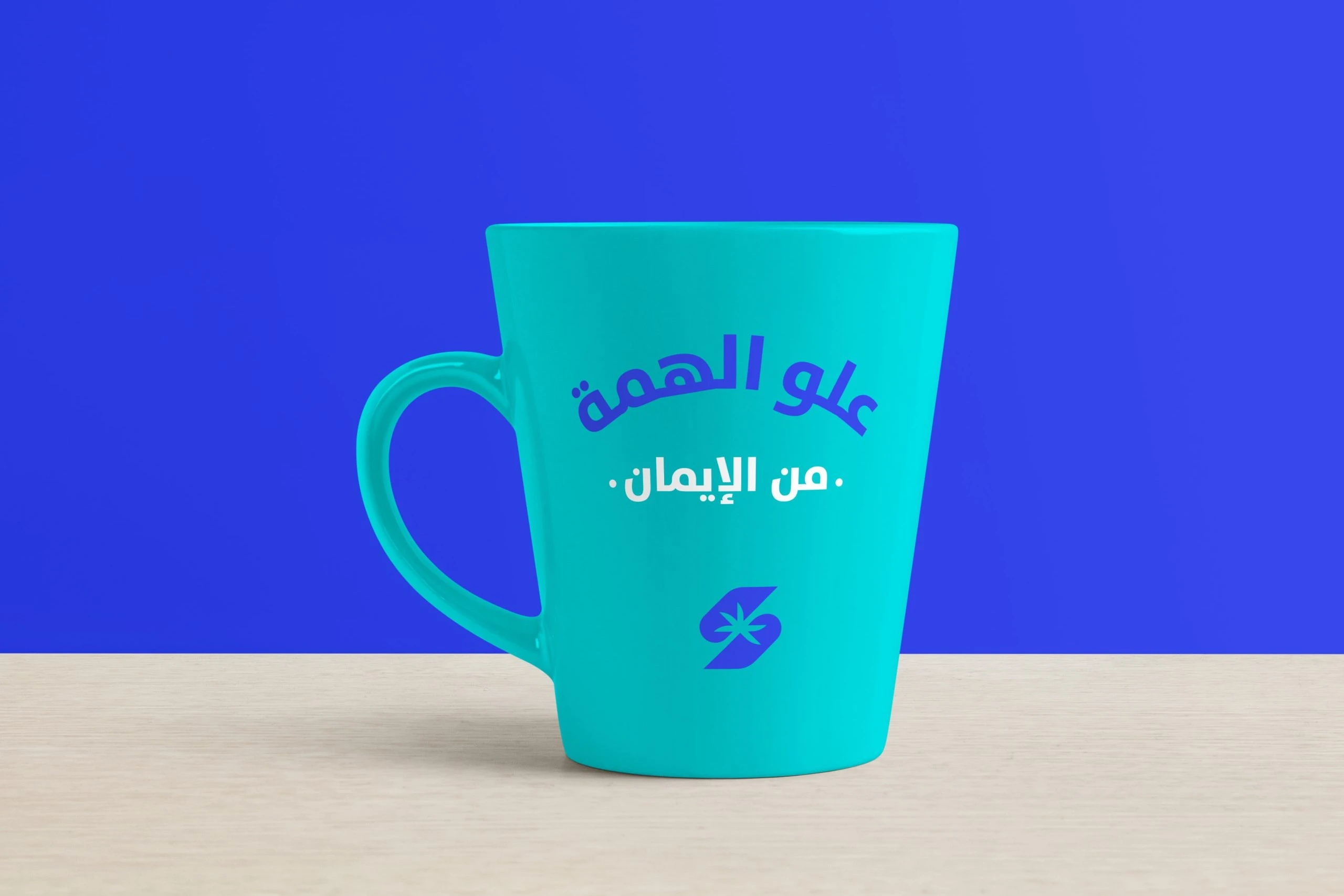 A turquoise mug printed in blue with علو الهمة من الإيمان and the symbol, on royal blue.
