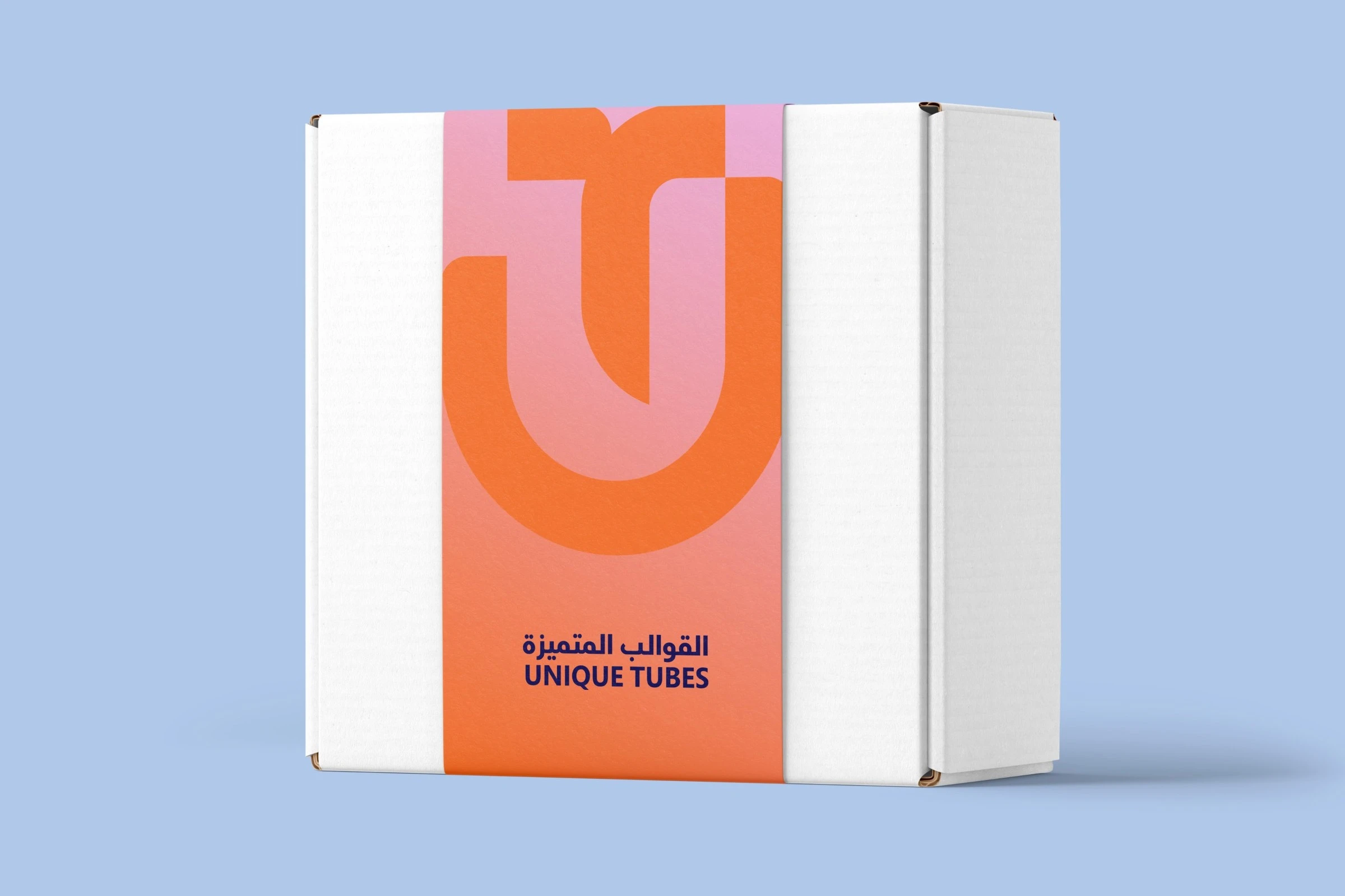A white box wrapped in a pink-to-orange sleeve with a large orange monogram and the bilingual logotype in dark blue, on pale blue.