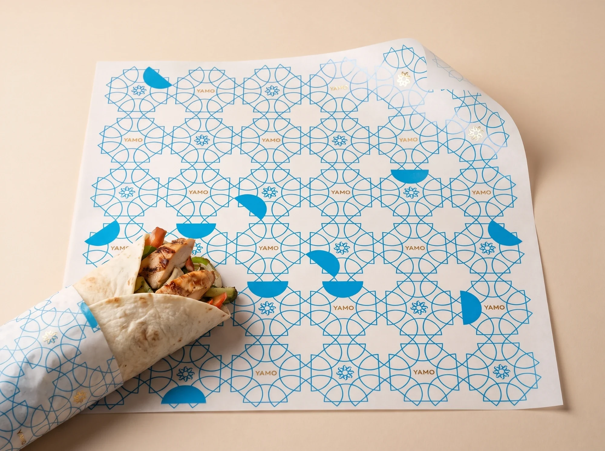Wrapping paper printed with the lattice in blue, the rosette and YAMO, and blue half-moons, around a chicken wrap.